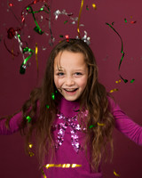 Young girl laughs as streamers fall around her against a pink studio backdrop