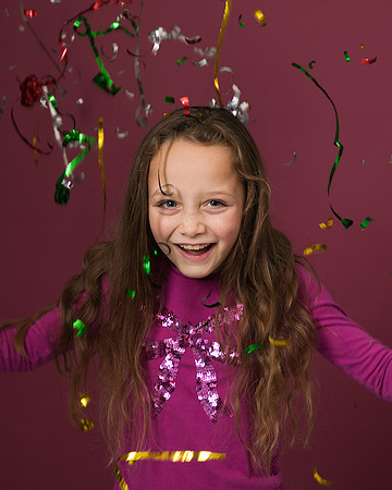 Young girl laughs as streamers fall around her against a pink studio backdrop