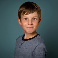 Boy dressed in blue smiles (without teeth) against a blue background