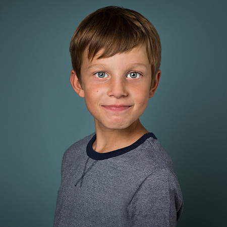 Boy dressed in blue smiles (without teeth) against a blue background