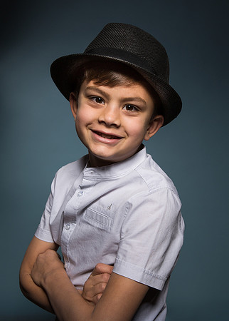 Trendy boy in hat & shirt smiles at camera against blue studio background