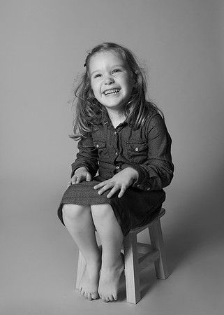 Girl sits on a stool and giggles, photographed in a studio sitting