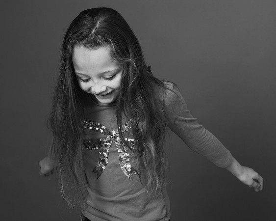 Pre-teen girl looks down and smiles, photographed in black & white in a studio