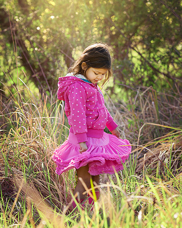 Little girl spins in long grass wearing a tutu with sunlight lighting her