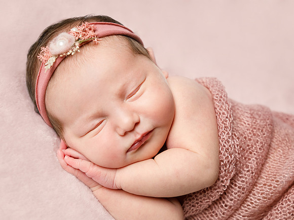 Newborn baby photographed asleep on her side with hands under her face on pink blankets