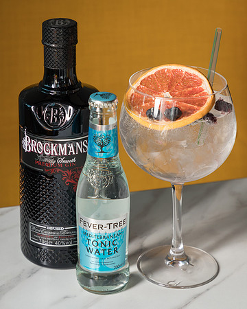 Gin and tonic bottles beside a gin glass photographed by a yellow background - on trend