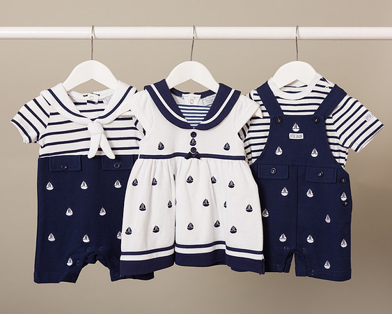Three sailor outfits for infants hung on a white rail
