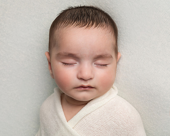 A close up of a sleeping baby's face, swaddled in a cream blanket