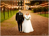 A bride and groom smile and walk together walking amongst fairy lights in the Beaumont Estate gardens in Old Windsor