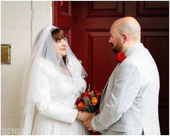 A wedding couple smile at each other outside Windsor Guildhall on a rainy day
