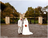 A wedding couple stand holding hands and smiling at each other with Windsor Castle in the background, photographed from the Long Walk