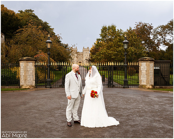 A wedding couple stand holding hands and smiling at each other with Windsor Castle in the background, photographed from the Long Walk