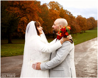 A wedding couple smile at each other hands on each others hips and shoulders, photographed close-up with autumnal trees on Windsor's Long Walk in the background
