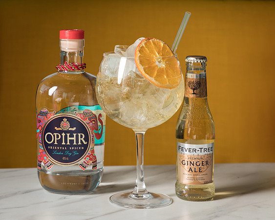 A photo of Opihr gin and tonic aside a gin glass against a yellow background