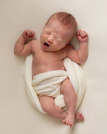 During her newborn photoshoot a baby girl on a cream background is stretching and yawning
