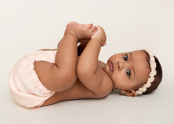 Baby girl lays on her back in pink nappy cover and headband