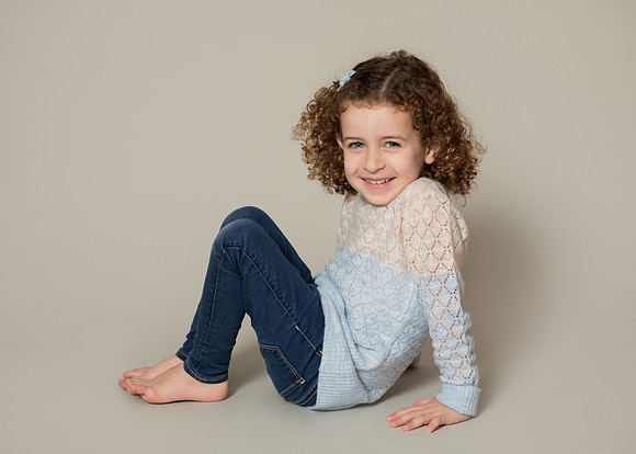 Young girl sits with her knees up smiling in a studio photograph