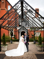 A bride and groom smile, framed by the glass porch at Macdonald Berystede Ascot