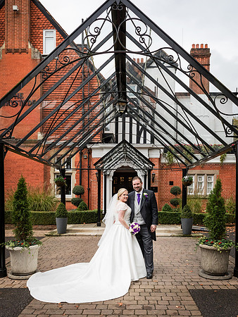 A bride and groom smile, framed by the glass porch at Macdonald Berystede Ascot