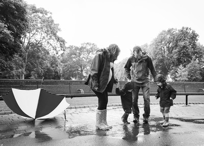 Family jump in puddles during rainy maternity photo session