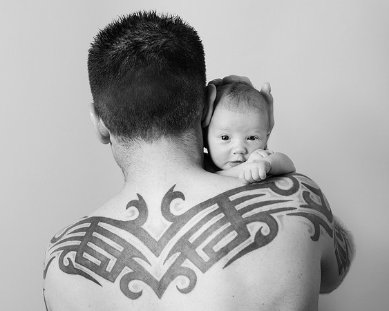 Newborn baby looks over dad's tattooed shoulder