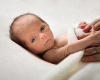 Premature baby looks at the camera with mum's hands comforting her