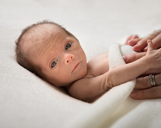 Premature baby looks at the camera with mum's hands comforting her