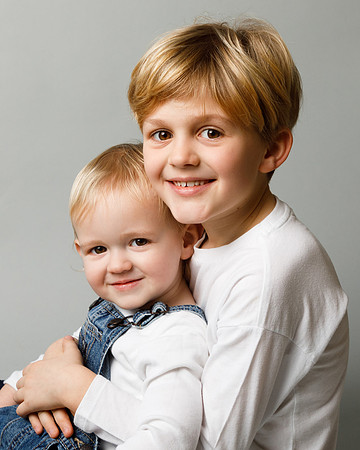An older brother hugs his toddler brother and both smile at the camera