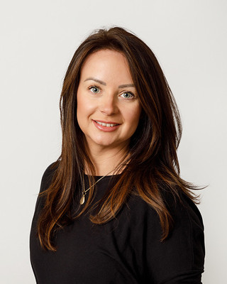 A smart businesswoman in dressed in black smiles at the camera in a studio setting with white backdrop