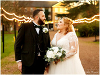 A bride and groom smile at each other lit by outdoor fairy lights all around them