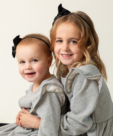 Two young sisters dressed in matching outfits in a close-up studio photograph