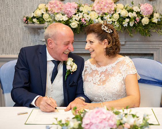 Bride & groom smile at each other whilst signing the wedding register