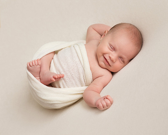 Baby boy wrapped in cream blanket smiles in his sleep