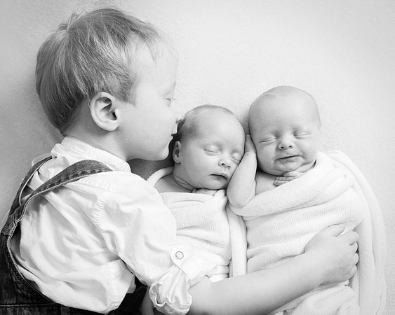 Toddler boy kisses and hugs his newborn twin baby siblings