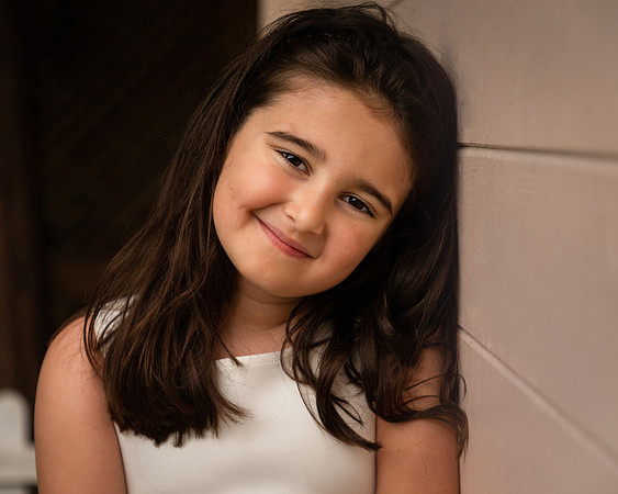 Girl smiles at camera whilst leaning against a pale pink fence