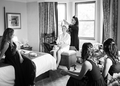 bride having hair and make up done as bridesmaids look on