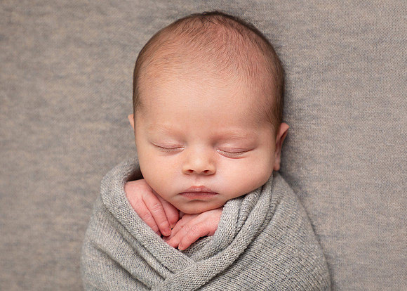 Newborn baby photographed fast asleep wrapped in grey