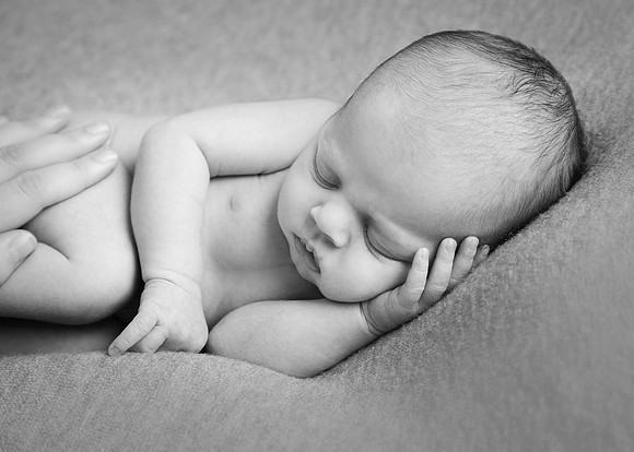 Baby laying asleep on his side with mum's hand comforting him