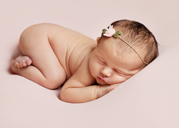 Baby laying on her front, posed during newborn photoshoot, on a pink blanket wearing a delicate flower headband