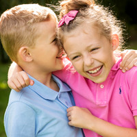 Close-up photo of a brother and sister giggling together in the sunshine