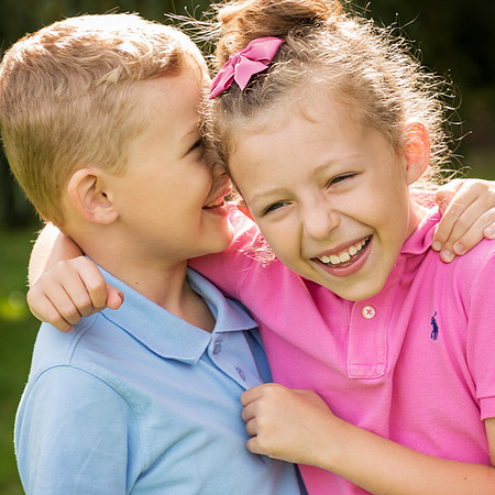 Close-up photo of a brother and sister giggling together in the sunshine