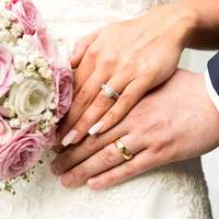 Close-up photo of bride & groom's hands with wedding rings on and holding bouquet