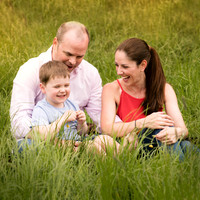 Family photographed laughing together sat amongst long grass