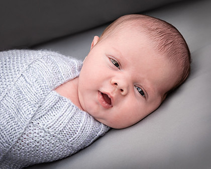 Newborn baby swaddled in blanket looks at camera with eyes wide open