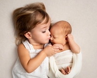 Baby brother swaddled in cream whilst being held by his big sister