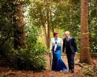 A bride and groom smile at each other whilst strolling through woodland at the Berystede in Ascot; the bride wears a stunning royal blue dress