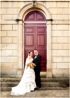 Wedding couple stand smiling in front of Windsor Guildhall's large red doors