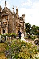 A wedding couple stand in front of gothic Oakley Court surrounded by wildflowers