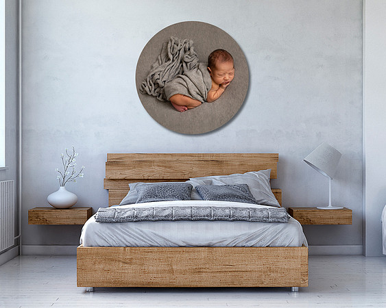 Bedroom with decoration on white hardwood floor with circular frame above the bed of a newborn baby laying on a grey blanket.