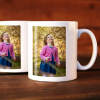 Two mugs with a photo on them of a girl dressed in pink and blue looking at trees, the mugs are sat on a table.